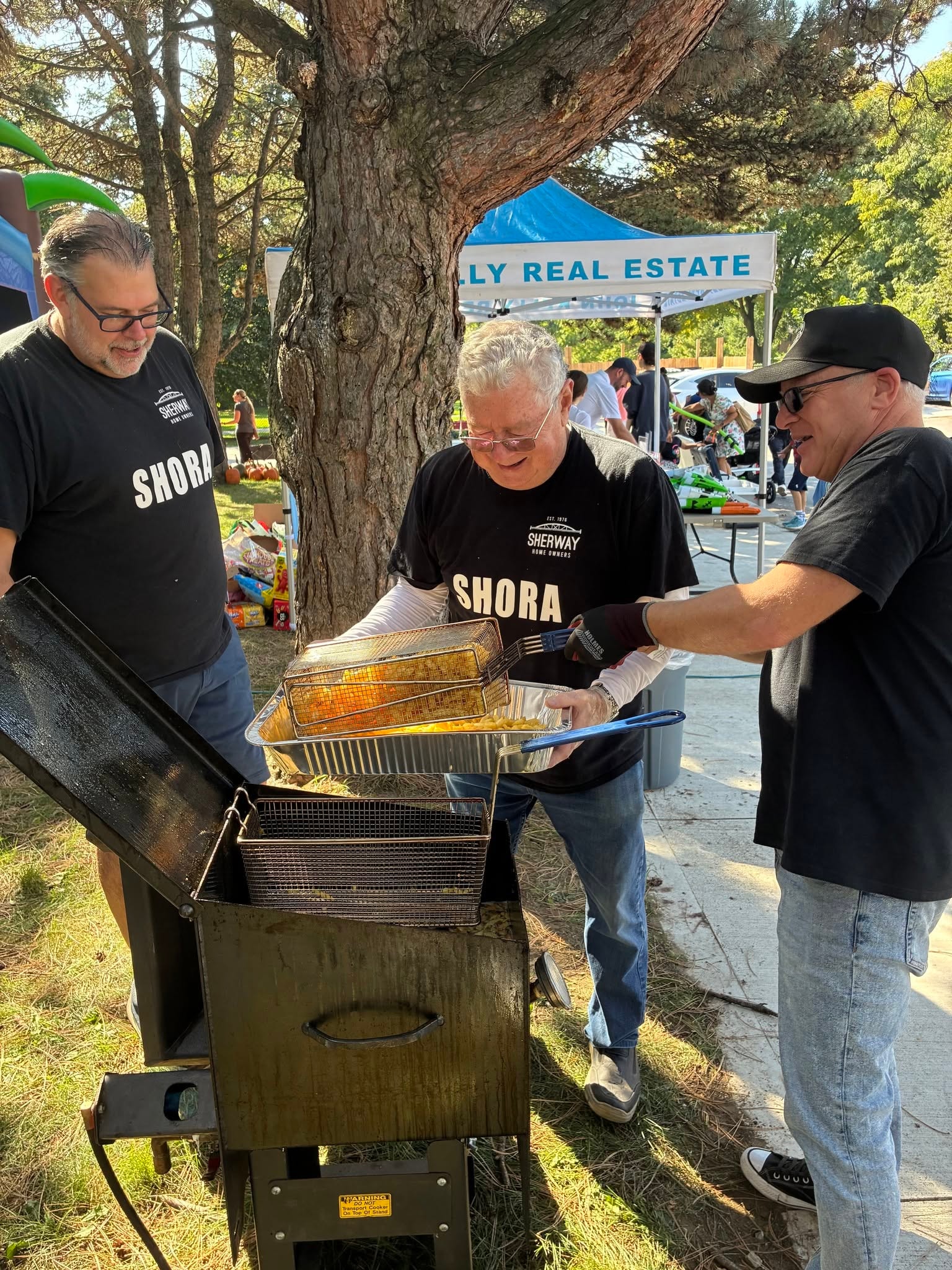 SHORA volunteers in SHORA shirts frying poutine at the outdoor fryer with John Kelly Real Estate tent in the background