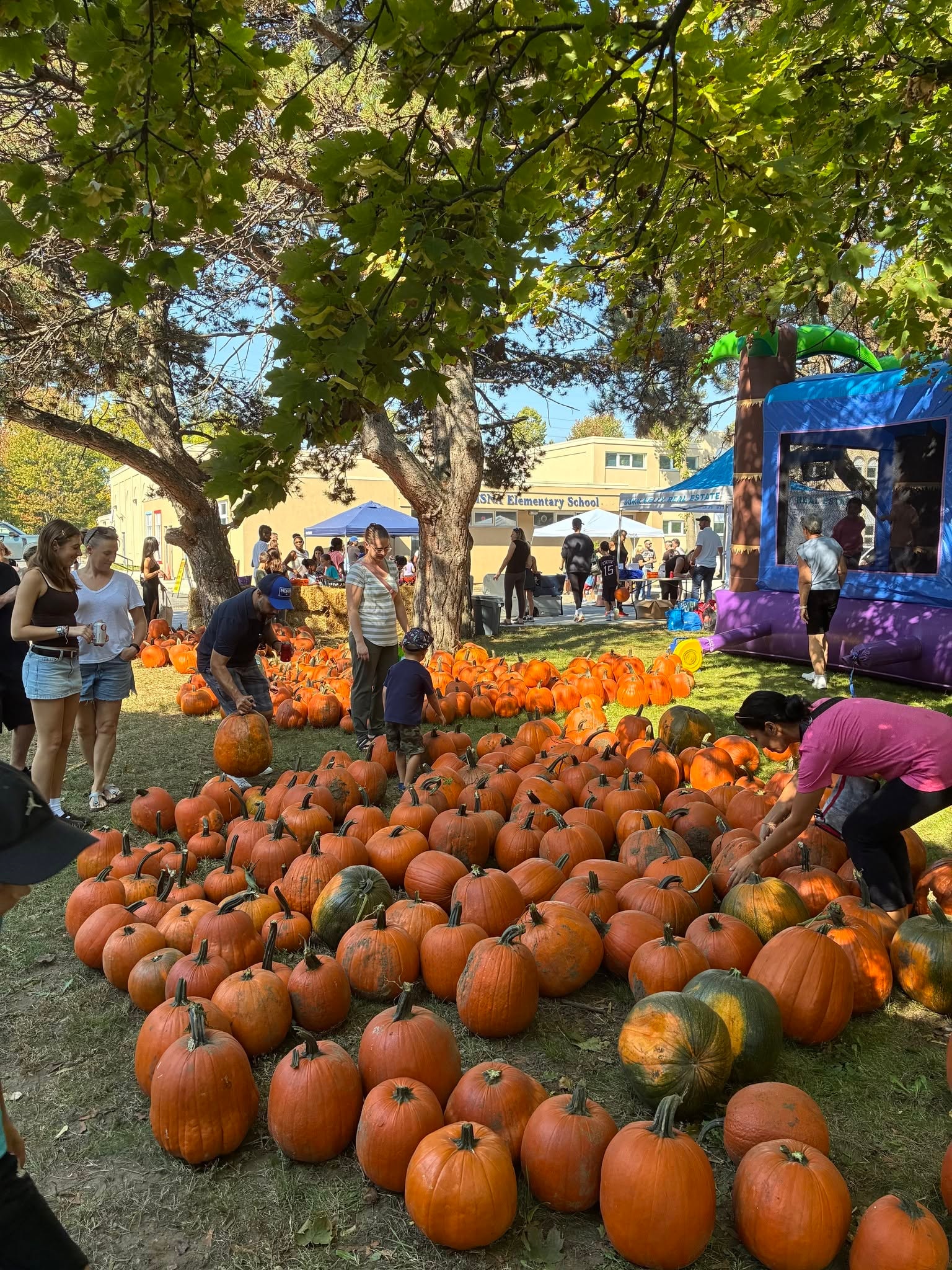Families picking pumpkins on the lawn at ISNA Elementary School with John Kelly Real Estate tent in the background