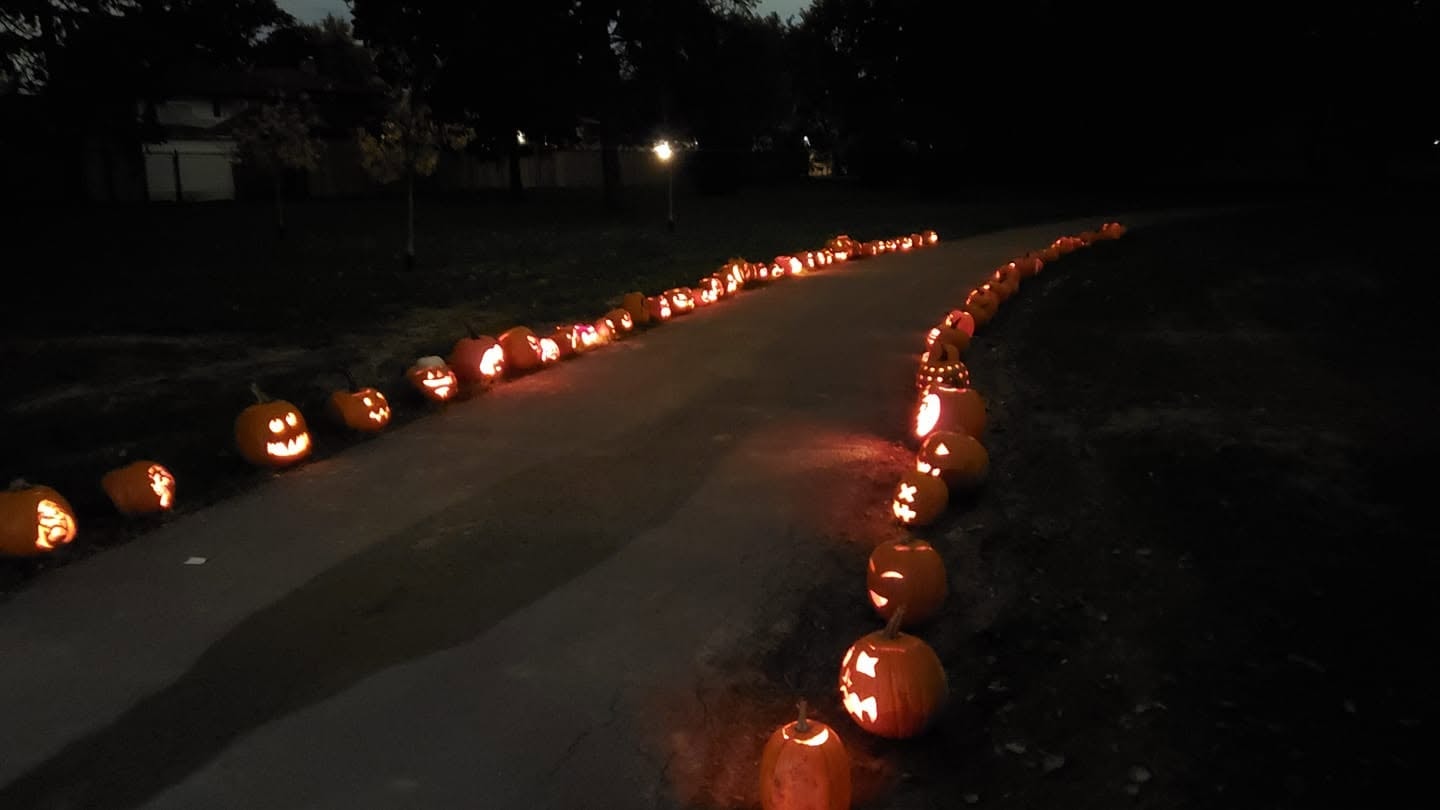 Dozens of glowing jack-o'-lanterns lining both sides of the pathway through Laughton Heights Park at night